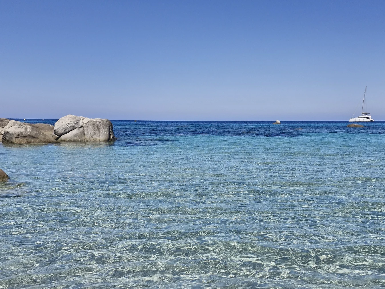 L&rsquo;horizon dégagé sur la mer, un voilier au loin et des rochers de granit, en Corse