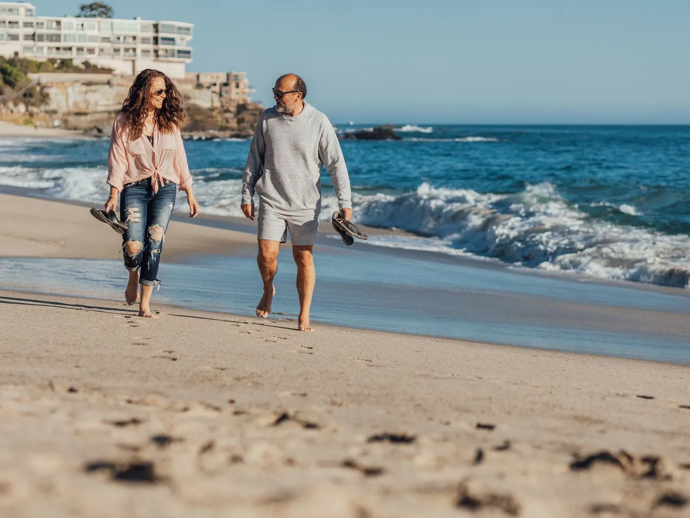 Un couple marche pieds nus sur la plage, dans la lumière