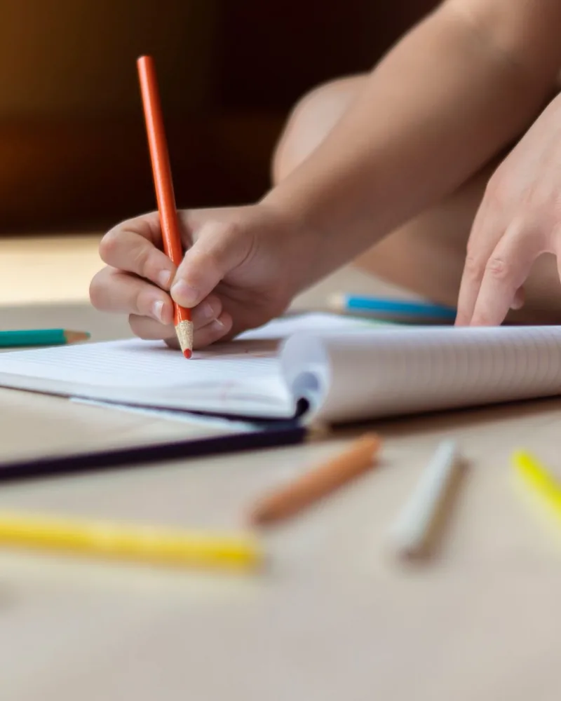 Un enfant dessine, entouré de crayons de couleur