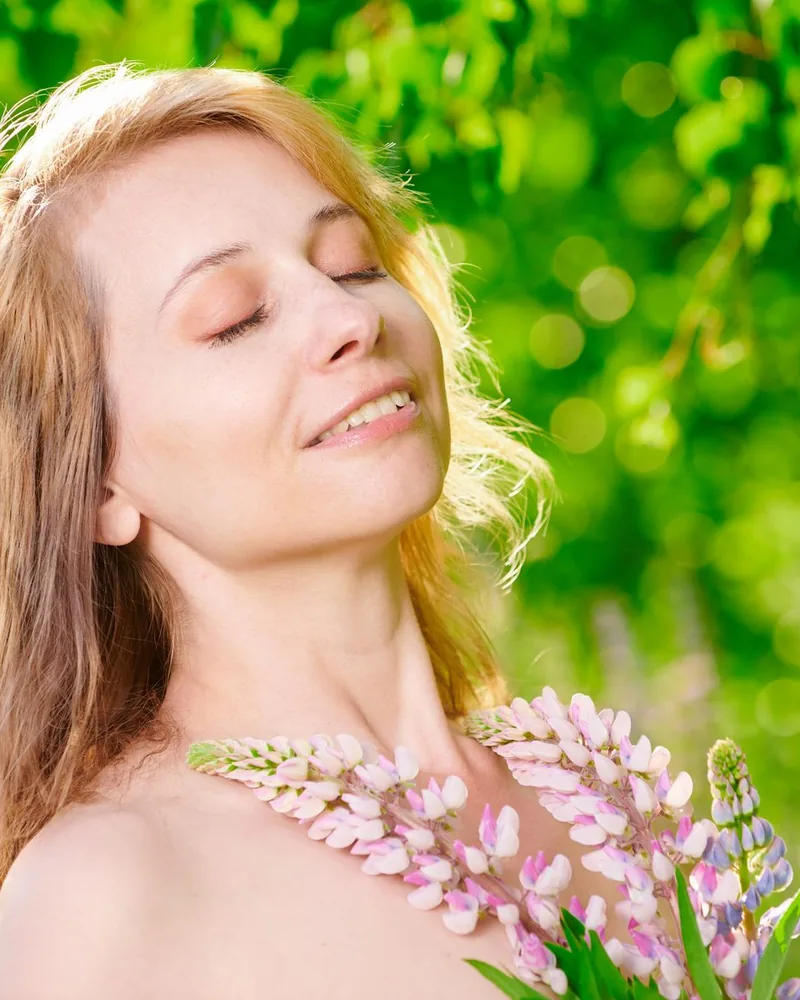 Une femme sourit, un bouquet de fleurs à la main, dans un jardin ensoleillé